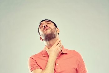 people, healthcare and problem concept - unhappy man touching his neck and suffering from throat pain over gray background. man touching neck and suffering from throat pain