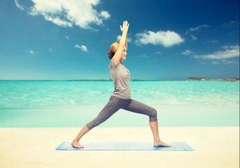 fitness, sport, people and healthy lifestyle concept - woman making yoga warrior pose on mat over beach background. woman making yoga warrior pose on mat