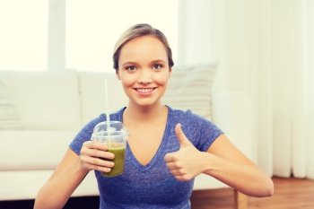 people, diet  and healthy lifestyle concept - happy woman with cup of smoothie at home and showing thumbs up. happy woman with cup of smoothie showing thumbs up