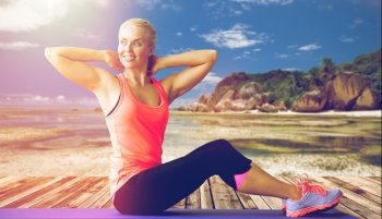 fitness, sport, training and people concept - smiling woman exercising on mat outdoors over exotic tropical beach background. smiling woman exercising on mat outdoors