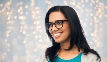 vision, portrait and people concept - happy smiling young indian woman in glasses over holidays lights background. happy smiling young indian woman in glasses