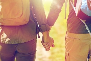 travel, hiking, backpacking, tourism and people concept - close up of couple with backpacks holding hands and walking along country road. close up of couple with backpacks holding hands