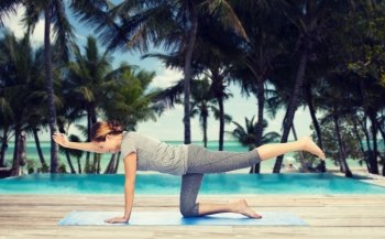 fitness, sport, people and healthy lifestyle concept - woman making yoga in balancing table pose on mat over hotel resort pool on tropical beach background. woman making yoga in balancing table pose on mat