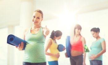 pregnancy, sport, fitness, people and healthy lifestyle concept - happy pregnant woman with mat in gym showing thumbs up . pregnant woman with mat in gym showing thumbs up 