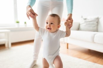 family, child, childhood and parenthood concept - happy little baby learning to walk with mother help at home. happy baby learning to walk with mother help