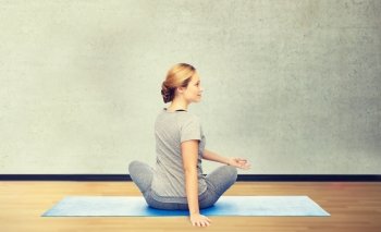 fitness, sport, people and healthy lifestyle concept - woman making yoga in twist pose on mat over gym room background. woman making yoga in twist pose on mat