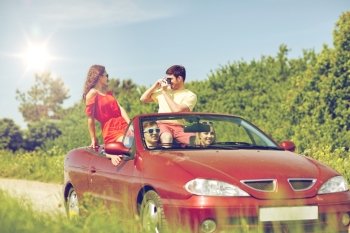 leisure, road trip, travel, summer holidays and people concept - happy friends driving in cabriolet car and taking picture by film camera. happy friends with camera driving in cabriolet car