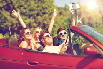 leisure, road trip, travel and people concept - happy friends driving in cabriolet taking picture by smartphone selfie stick at country. friends driving in cabriolet car and taking selfie