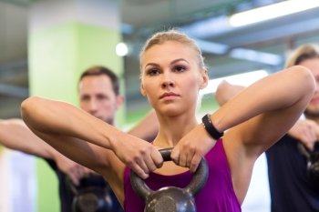 sport, fitness, weightlifting and people concept - woman with kettlebell and heart-rate tracker at group training exercising in gym. group of people with kettlebells exercising in gym