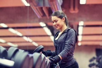 fitness, sport, exercising, weightlifting and people concept - young smiling woman choosing dumbbells in gym. young smiling woman choosing dumbbells in gym