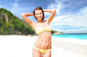 people, summer holidays, vacation and travel concept - happy smiling young woman posing in bikini swimsuit posing with raised hands over exotic tropical beach and sea shore background. happy woman in bikini swimsuit on tropical beach