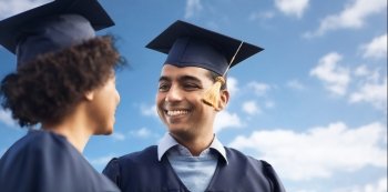 education, graduation and people concept - happy international students in mortar boards and bachelor gowns over blue sky and clouds background. happy students or bachelors over blue sky. happy students or bachelors over blue sky