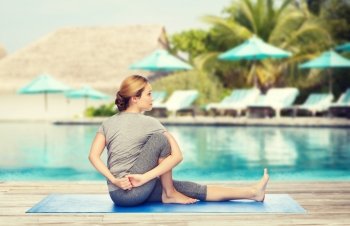 fitness, sport, people and healthy lifestyle concept - woman making yoga in twist pose on mat over beach and swimming pool background. woman making yoga in twist pose on mat. woman making yoga in twist pose on mat