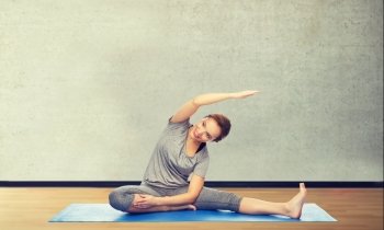 fitness, sport, people and healthy lifestyle concept - happy woman making yoga and stretching on mat over gym room background. happy woman making yoga and stretching on mat. happy woman making yoga and stretching on mat