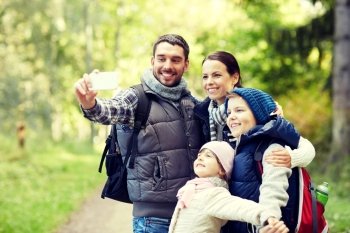 travel, tourism, hike, technology and people concept - happy family with backpacks taking selfie by smartphone in woods. family taking selfie with smartphone in woods. family taking selfie with smartphone in woods