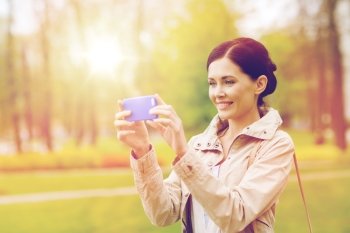 drinks, leisure, technology and people concept - smiling woman taking picture with smartphone in park. smiling woman taking picture with smartphone. smiling woman taking picture with smartphone