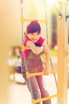 summer, childhood, leisure and people concept - happy little girl on children playground climbing by rope-ladder. happy little girl climbing on children playground. happy little girl climbing on children playground