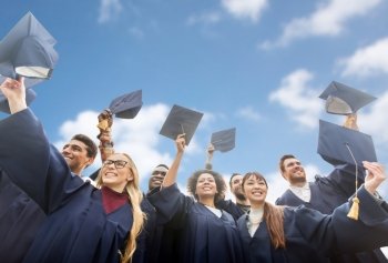 education, graduation and people concept - group of happy international students in bachelor gowns waving mortar boards or hats over blue sky and clouds background. happy bachelors waving mortar boards over sky. happy bachelors waving mortar boards over sky