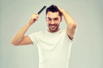 beauty, grooming and people concept - smiling young man brushing hair with comb over gray background. happy man brushing hair with comb over gray. happy man brushing hair with comb over gray