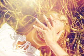 nature, summer holidays, vacation and people concept - close up of happy young woman lying on cereal field and covering face by hand. happy young woman lying on cereal field. happy young woman lying on cereal field