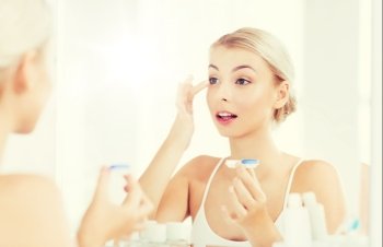 beauty, vision, eyesight, ophthalmology and people concept - young woman putting on contact lenses at mirror in home bathroom. young woman putting on contact lenses at bathroom. young woman putting on contact lenses at bathroom