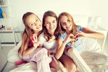 friendship, people, pajama party and technology concept - happy friends or teenage girls with monopod taking selfie at home. teen girls with selfie stick photographing at home