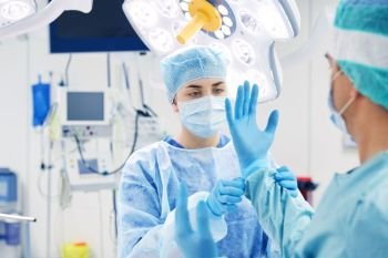 surgery, medicine and people concept - nurse assisting surgeon and helping with gloves in operating room at hospital. surgeons in operating room at hospital