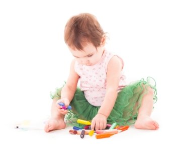 Toddler girl draws with 
wax crayons on the paper