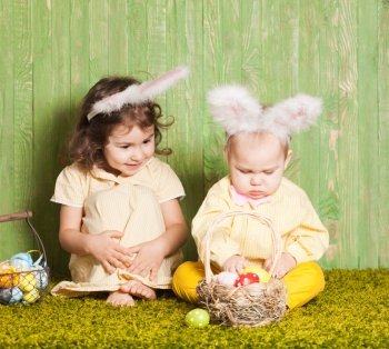Little boy and girl as a Easter rabbits on the grass with colorful eggs. Easter rabbits babies
