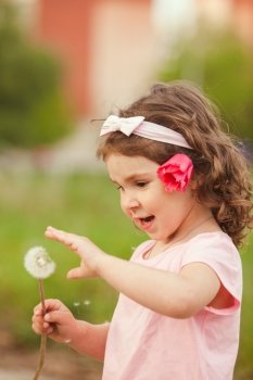 The little girl with a red flower in her hair played with dandelion. Curly girl with dandelion