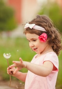 The little girl with a red flower in her hair played with dandelion. Curly girl with dandelion