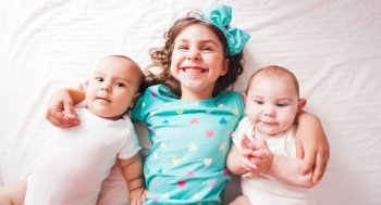Five years old girl with her brothers - twins lying on the bed. Sister with twins