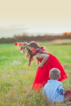 Cute girl is trying to put a floral wreath on her brother head. Brother and sister