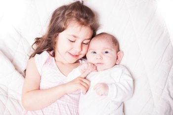 Pretty little girl laying with her adorable brother on the soft background. Sister with brother