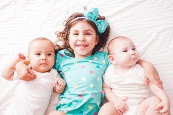 Five years old girl with her brothers - twins lying on the bed. Sister with twins
