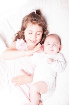 Pretty little girl laying with her adorable brother on the soft background. Sister with brother