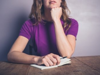 A thoughtful young woman is writing in a notepad at a table