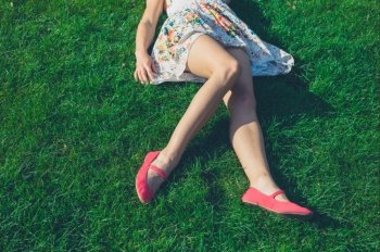 The legs and feet of a young woman wearing a dress as she is relaxing on the grass on a sunny summer day