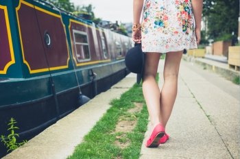 A young woman is walking along the canal on a sunny day in summer and is passing a houseboat