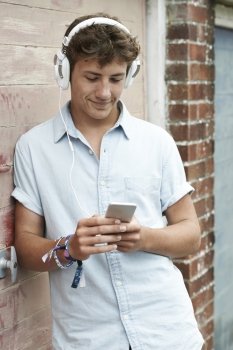 Teenage Boy Wearing Headphones And Listening To Music In Urban Setting