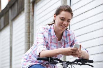 Teenage Girl In Urban Setting Using Mobile Phone Whilst Riding Bike