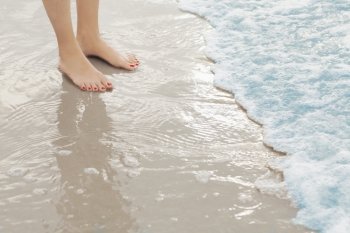 Woman’s feet standing in surf at the beach