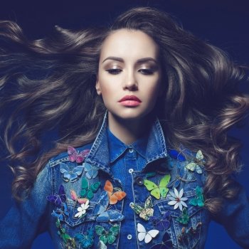 Fashion studio photo of young beauty woman  with a lot of brooches on her jeans jacket. Denim clothes. Jeans trend. Magnificent hair