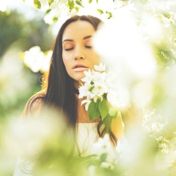 Outdoor fashion photo of beautiful young woman surrounded by flowers of apple-tree. Spring blossom