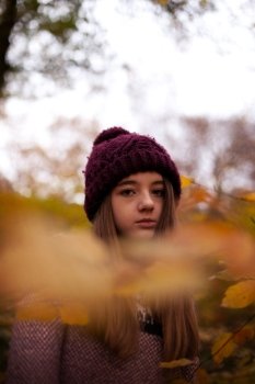 Pretty young girl looking Autumnal through leaves in a forrest