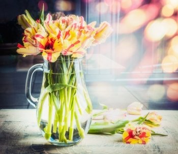 Bright  bouquet of tulips in glass jug on table at sunny spring day background with bokeh, front view