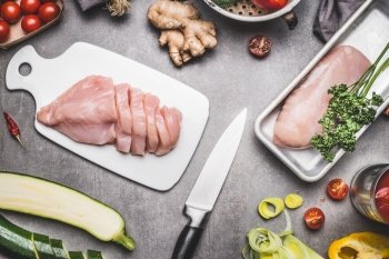 Chicken breast preparation with cut vegetables ingredients, knife and cutting board, on gray concrete background, top view, flat lay.  Healthy or diet food concept