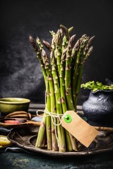 Asparagus bunch with blank tag on dark rustic kitchen table, front view