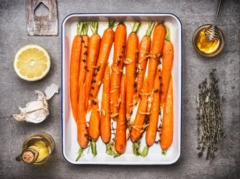 Carrots with thyme, garlic, lemon and honey on baking tray , cooking preparation with ingredients, top view. Healthy root vegetables concept