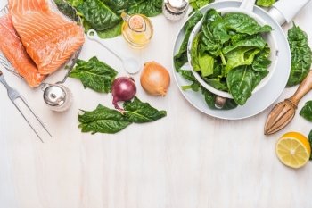 Spinach leaves and salmon fillets  with ingredients on white kitchen table background, cooking preparation, top view, border. Diet  nutrition and healthy food concept